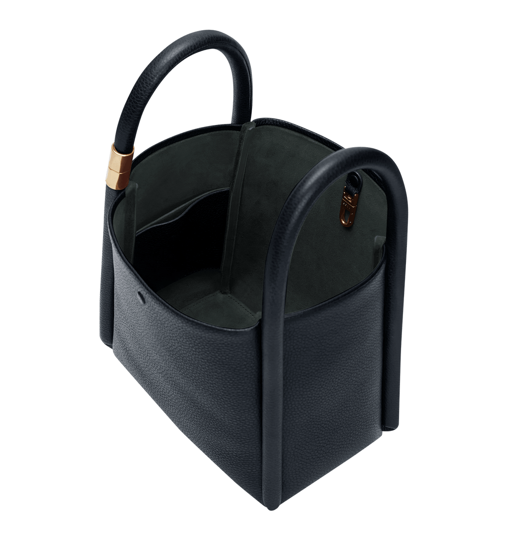 Blue, pebbled leather bag. Features oversized piping detail, an open top, intertwined handles, a subtle gold fastener, and a leather carrying strap.